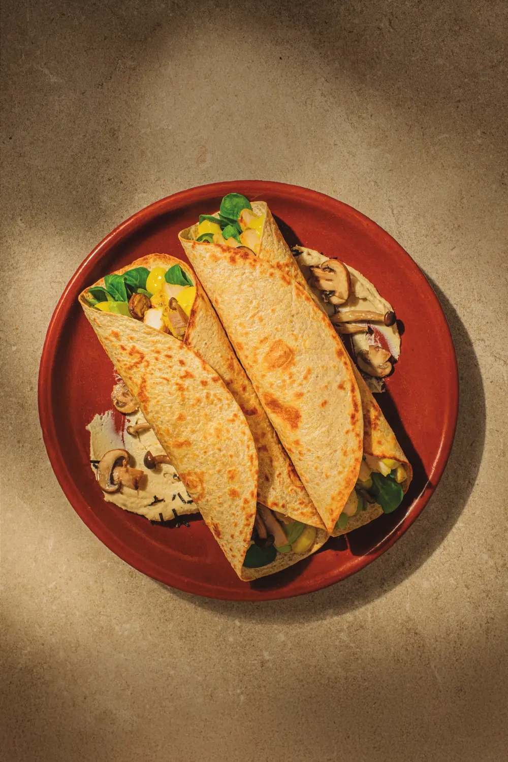 Two Deli Sun wheat wraps filled with vegetables and mushrooms on a clay plate